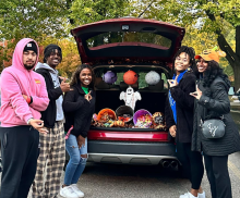 NPHC leaders standing next to Halloween decorated trunk of car handing out candy.